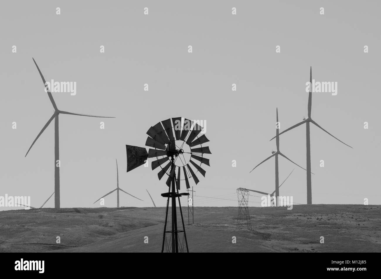 A vintage windmill provides a contrast to a modern wind farm with giant