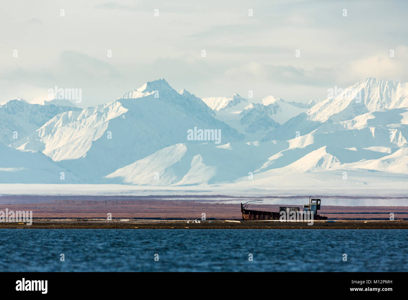 The Brooks Range looms large over a shipwrecked boat off Barter Island near Kaktovik in the Arctic National Wildlife Refuge in Alaska. Stock Photo