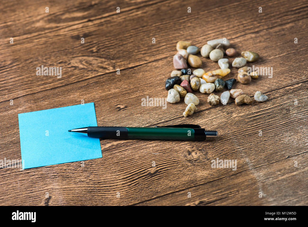 Pencil placed on post-it with many pebbles in wooden background Stock Photo