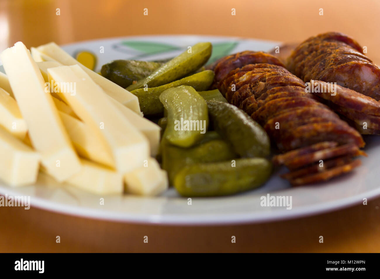 Plate with sliced cheese, gherkin or cucumber pickles and spicy sausage