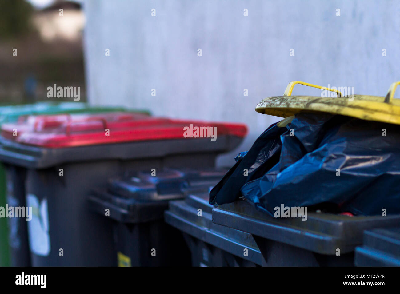 Row of overflowing rubbish bins with different colored lids and black bags of refuse. Stock Photo