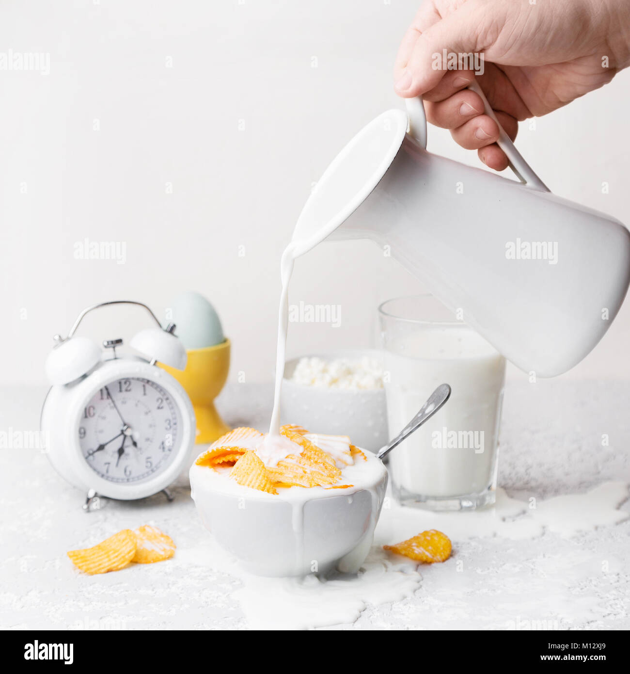 Man hand pouring milk to white bowl with heap of golden crispy potato chips on white background, copy space. Unhealthy food concept Stock Photo