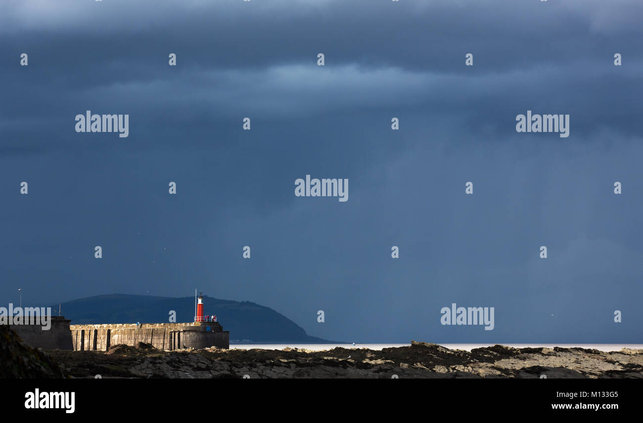 Watchet harbour lighthouse with stormy sky  from Hellwell Bay Stock Photo