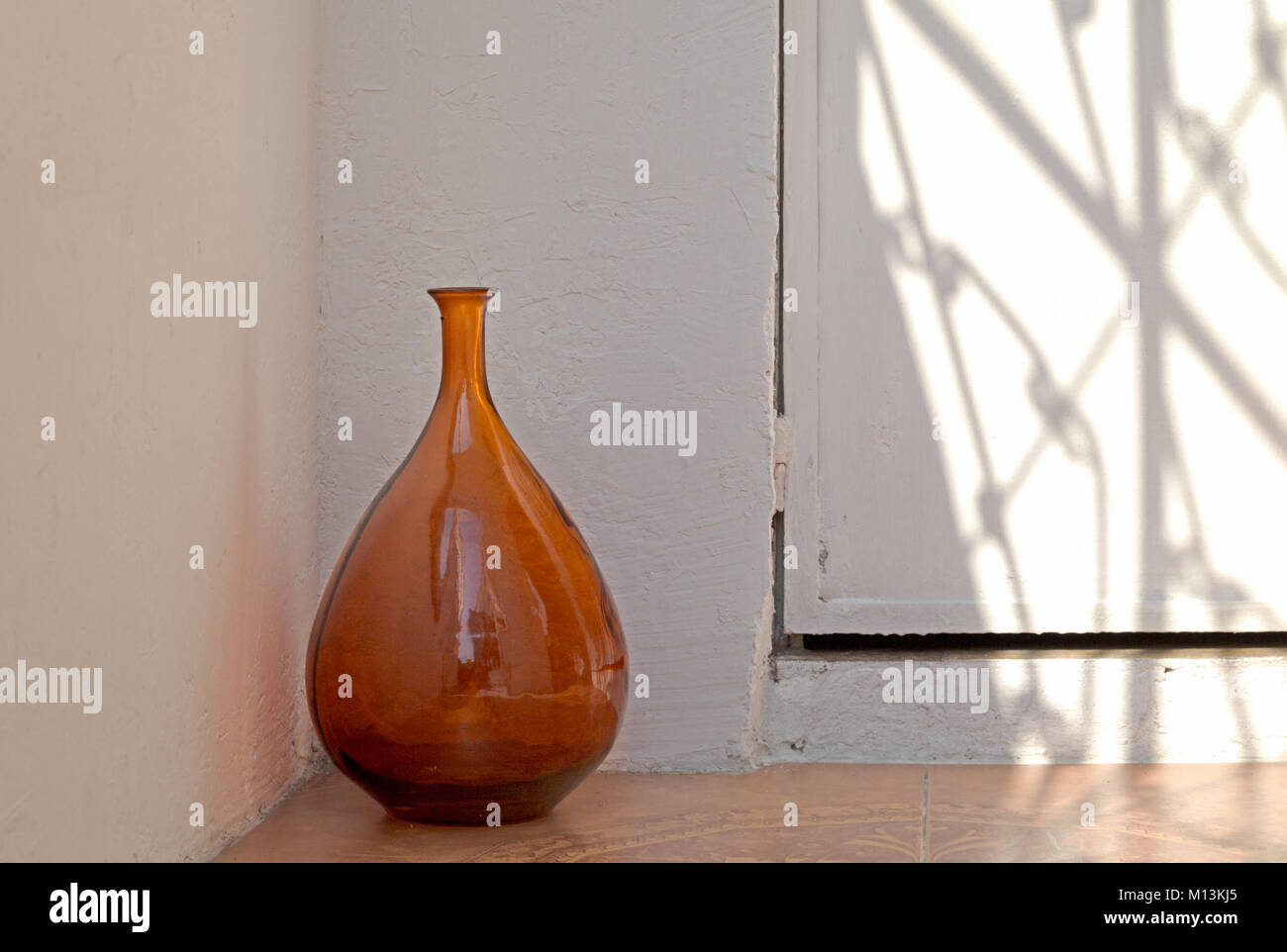 An orange brown colored glass vase sits corner of the shadow casting room, Mexico City, Mexico. Stock Photo
