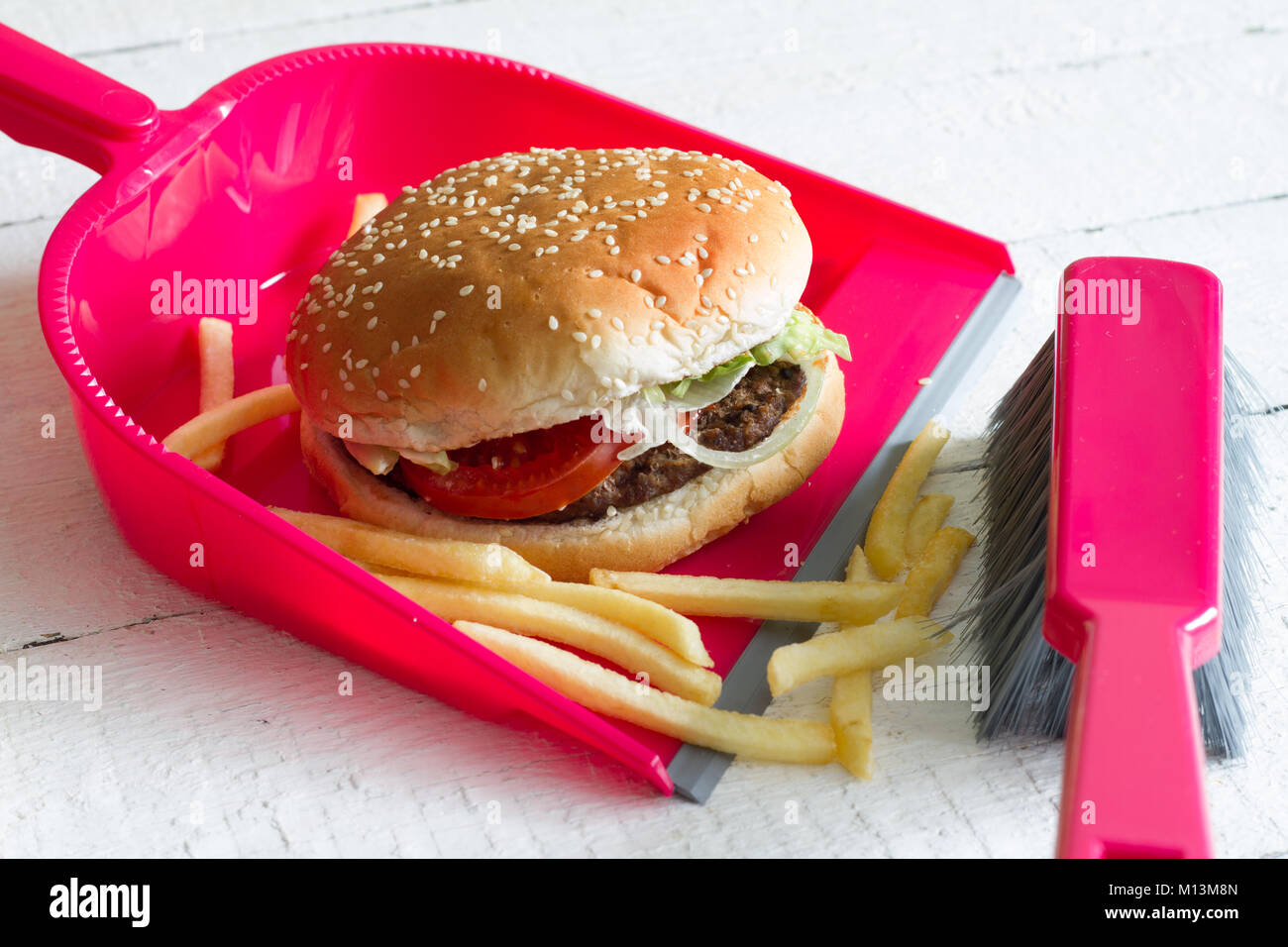 Sweeping junk food with burger chips and dustpan concept of health detox diet Stock Photo