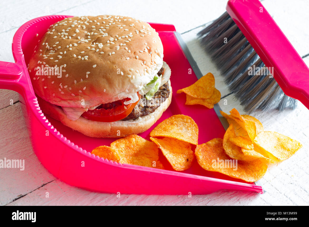Sweeping junk food with burger chips and dustpan concept of health detox diet Stock Photo