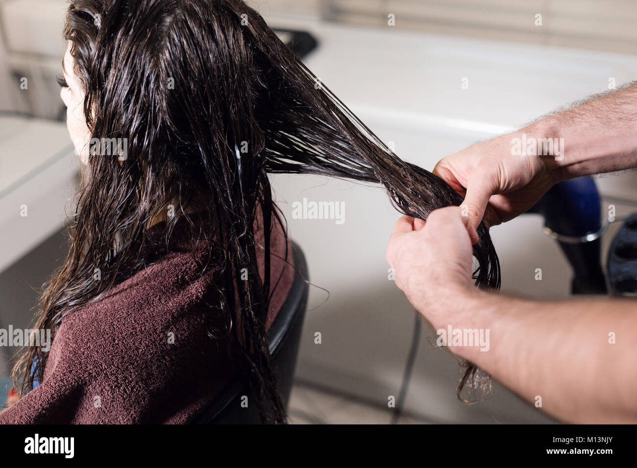 Closeup hairdresser man makes hairstyle for young woman in beauty salon