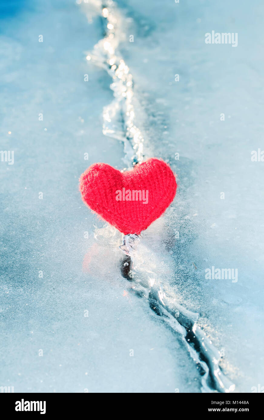 bright hot heart made of yarn lies on the clear blue cold ice and melted the deep crack Stock Photo
