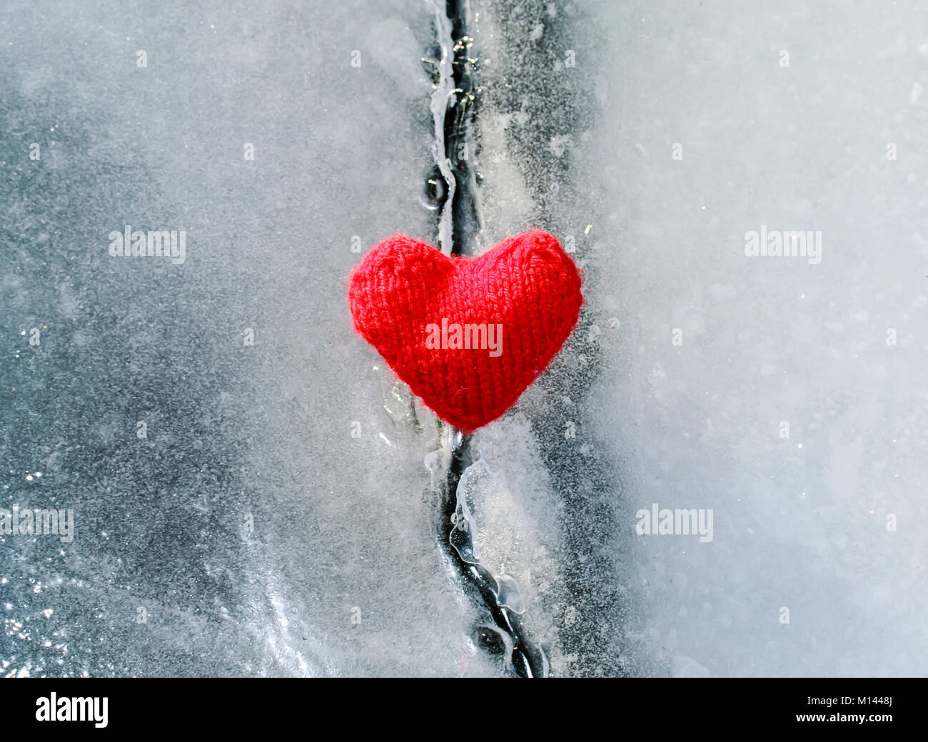 bright hot scarlet heart made of yarn lies on the clear blue cold ice and melted the deep crack Stock Photo