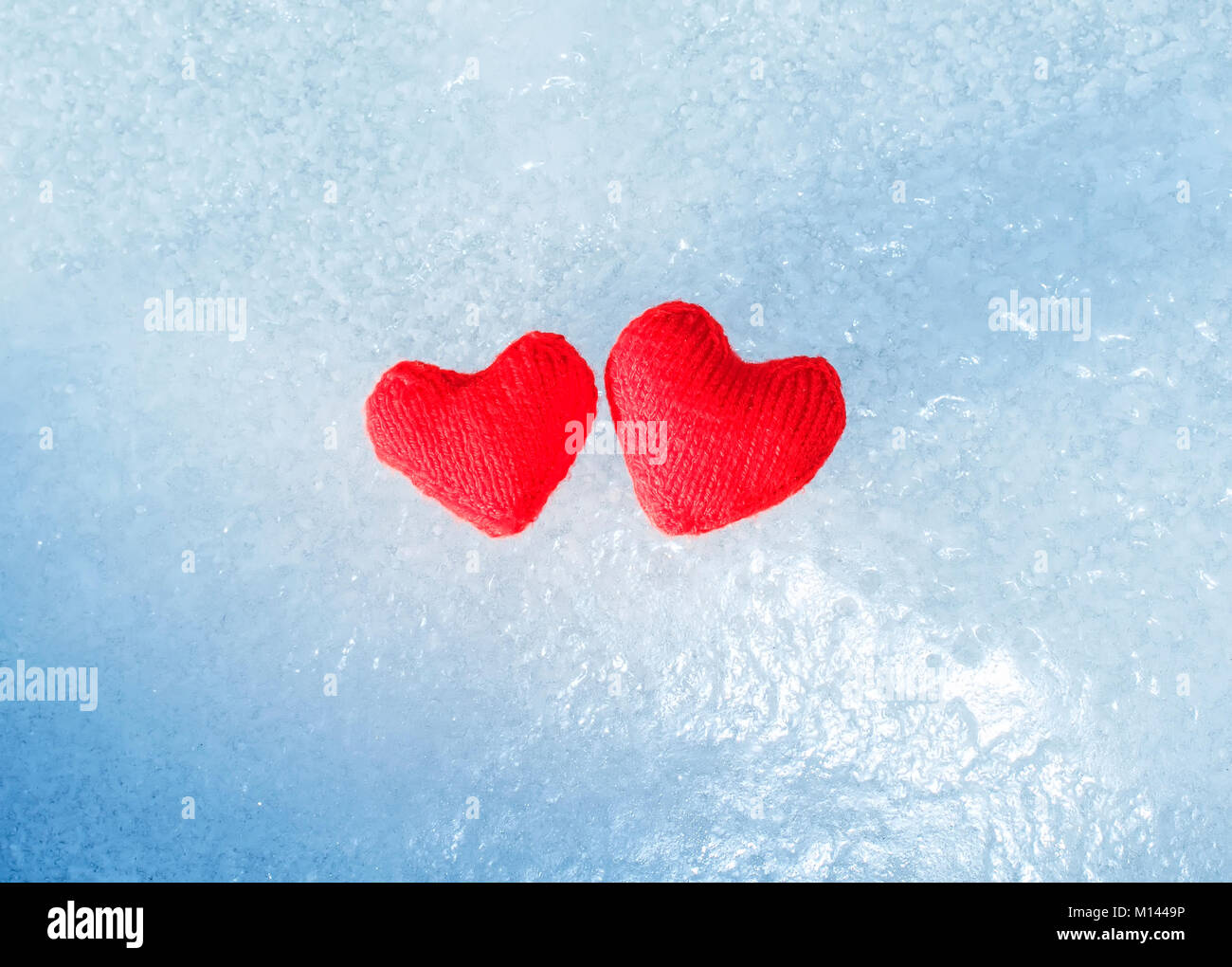 two bright red hot heart made of yarn lying on the cold transparent blue ice Stock Photo