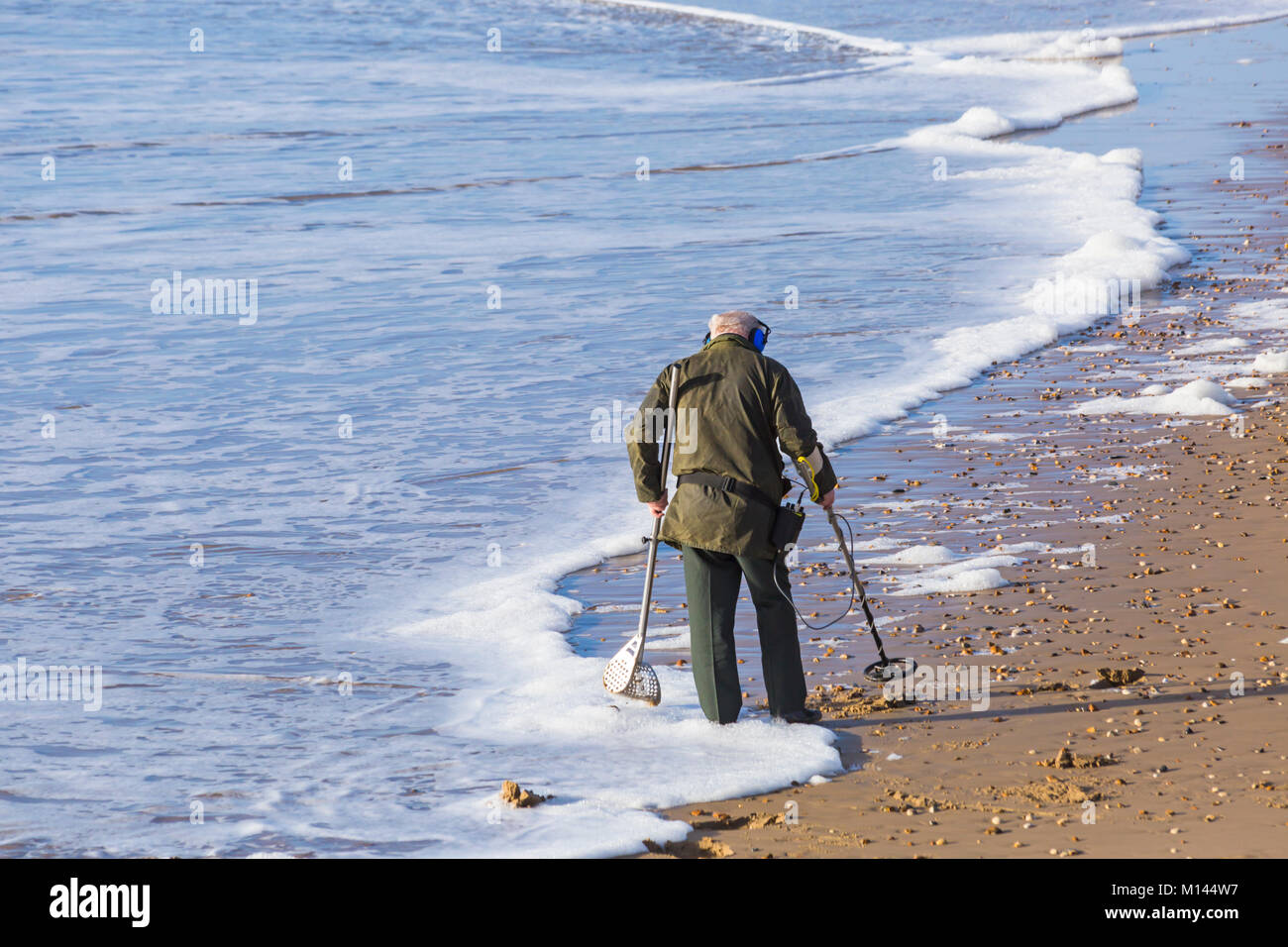 Beach comber with metal detector looking for treasure at Bournemouth beach, Bournemouth, Dorset UK in January Stock Photo