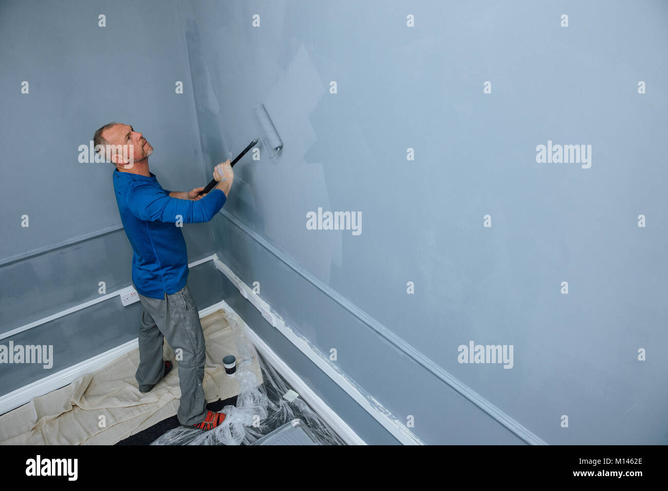 High Angle View Of A Male Builder Using A Roller To Paint Walls Of