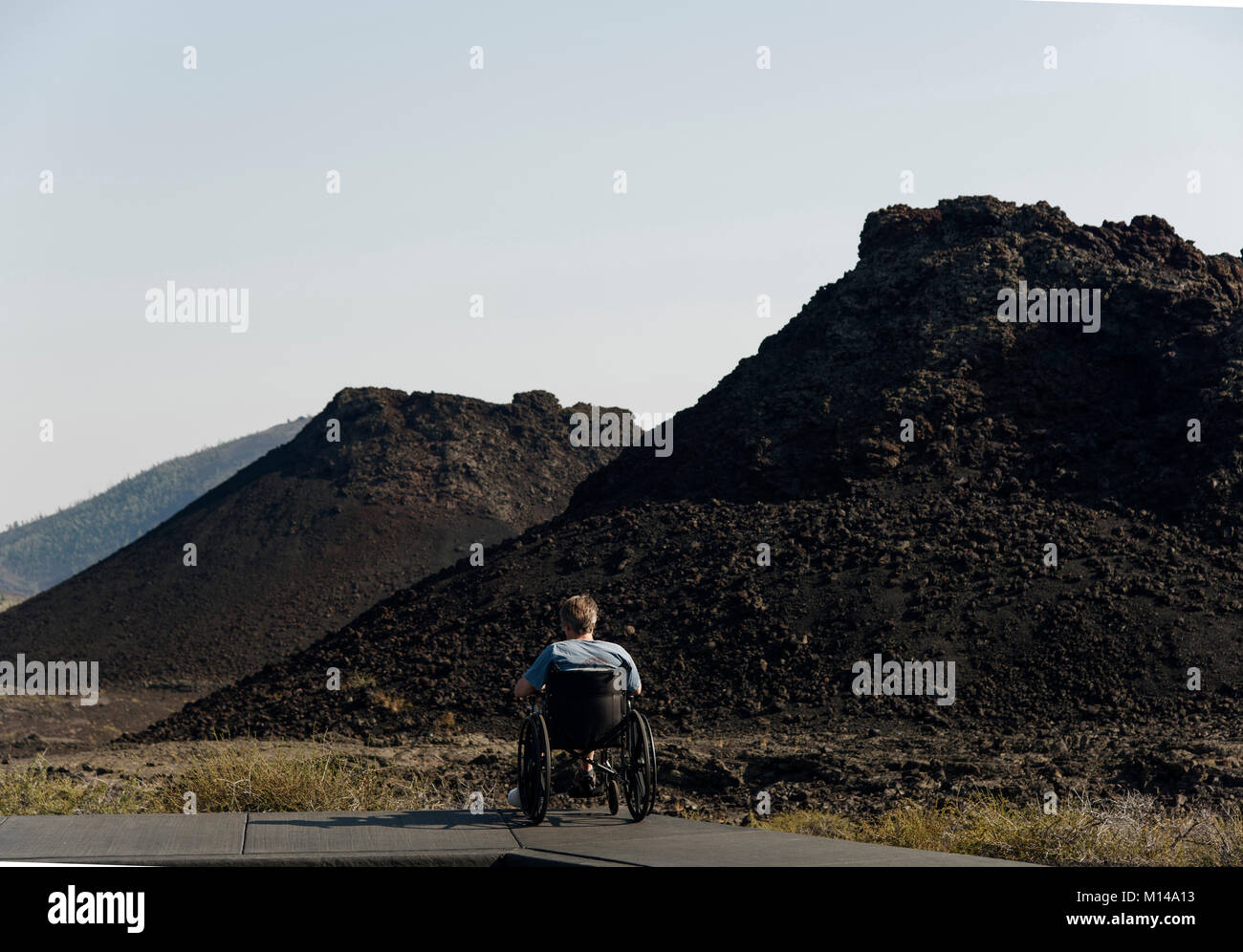A man in a wheelchair views the spatter cones at Craers of the Moon Natl. Monument, USA.  Fortunately, the top of the first cone is accessible to him. Stock Photo