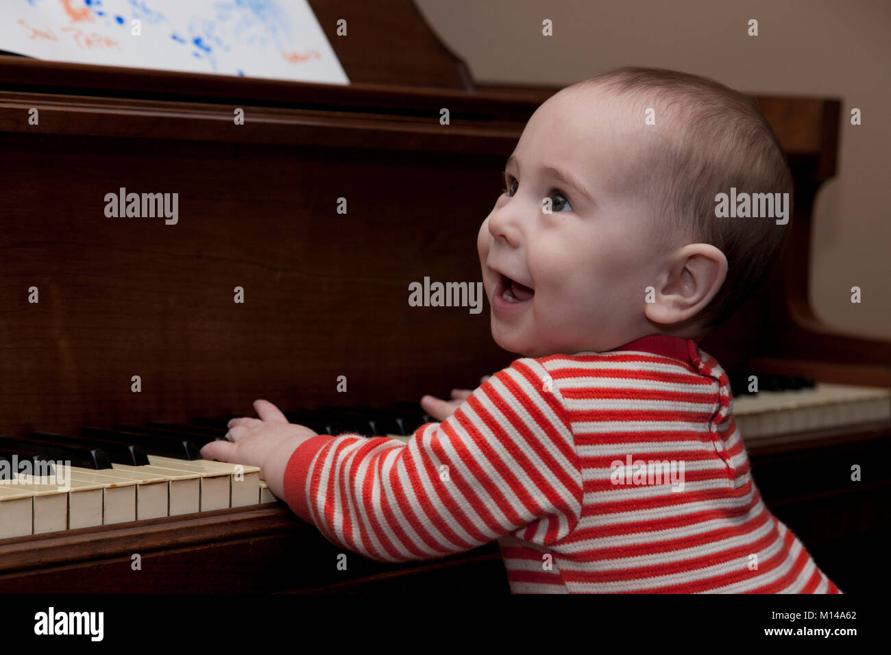 A happy toddler tries his hand on the keys of a piano. Stock Photo