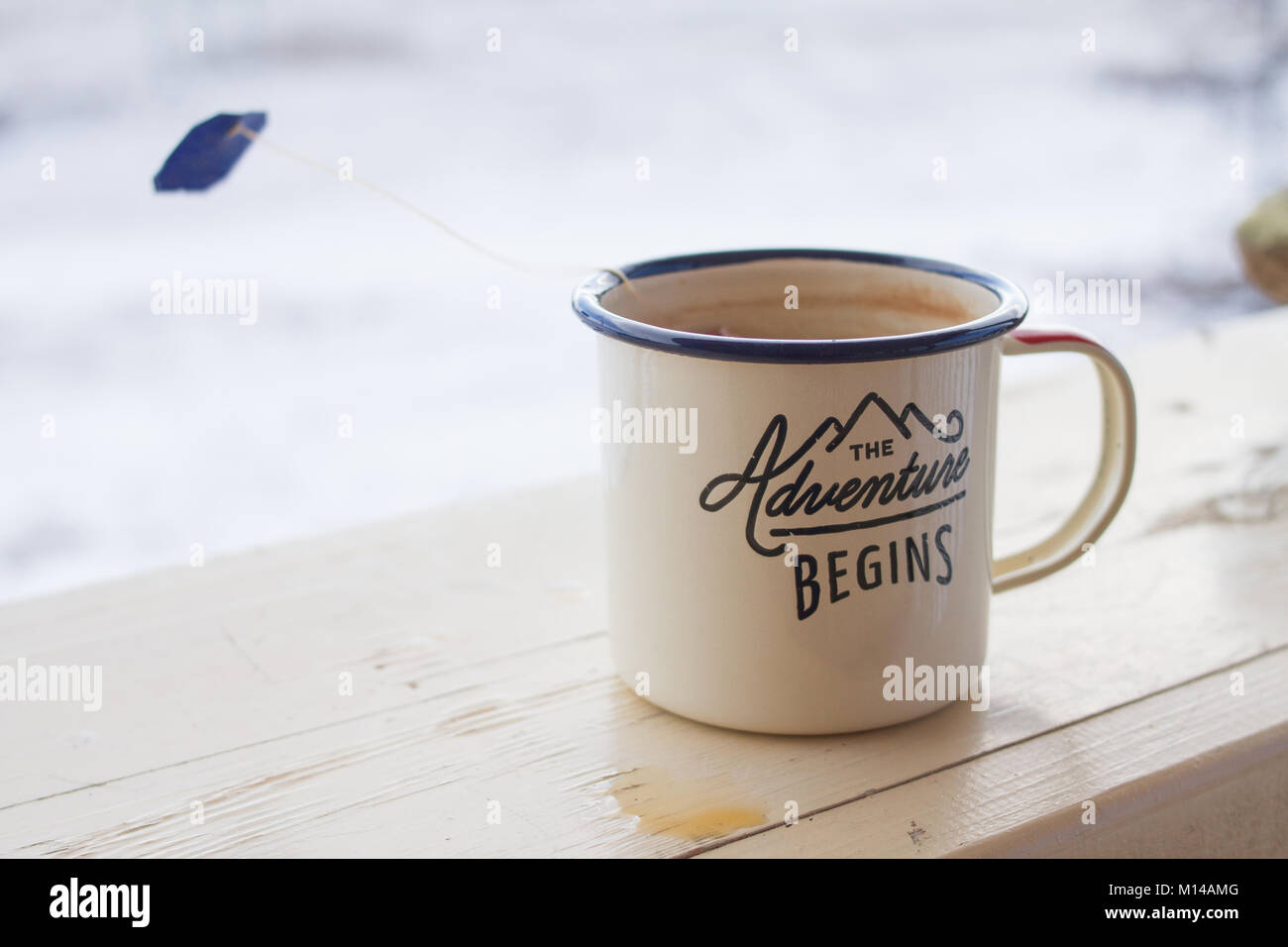 Enamel mug with strong tea and tea bag on a wooden fence on a snowy winter background. Stock Photo