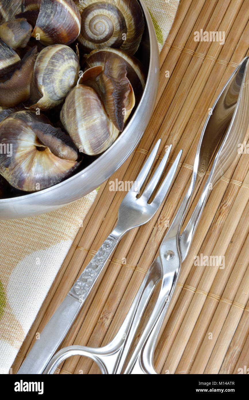 Cooked snails in bowl with tong and fork Stock Photo Alamy