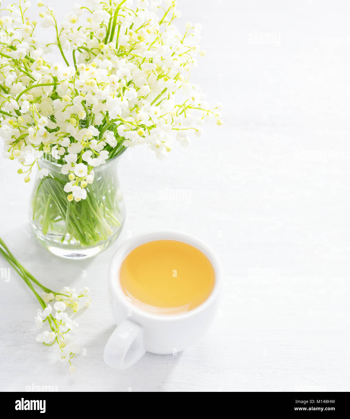 Bouquet of Lilies of the Valley and   cup of tea    on white wooden  table. Stock Photo