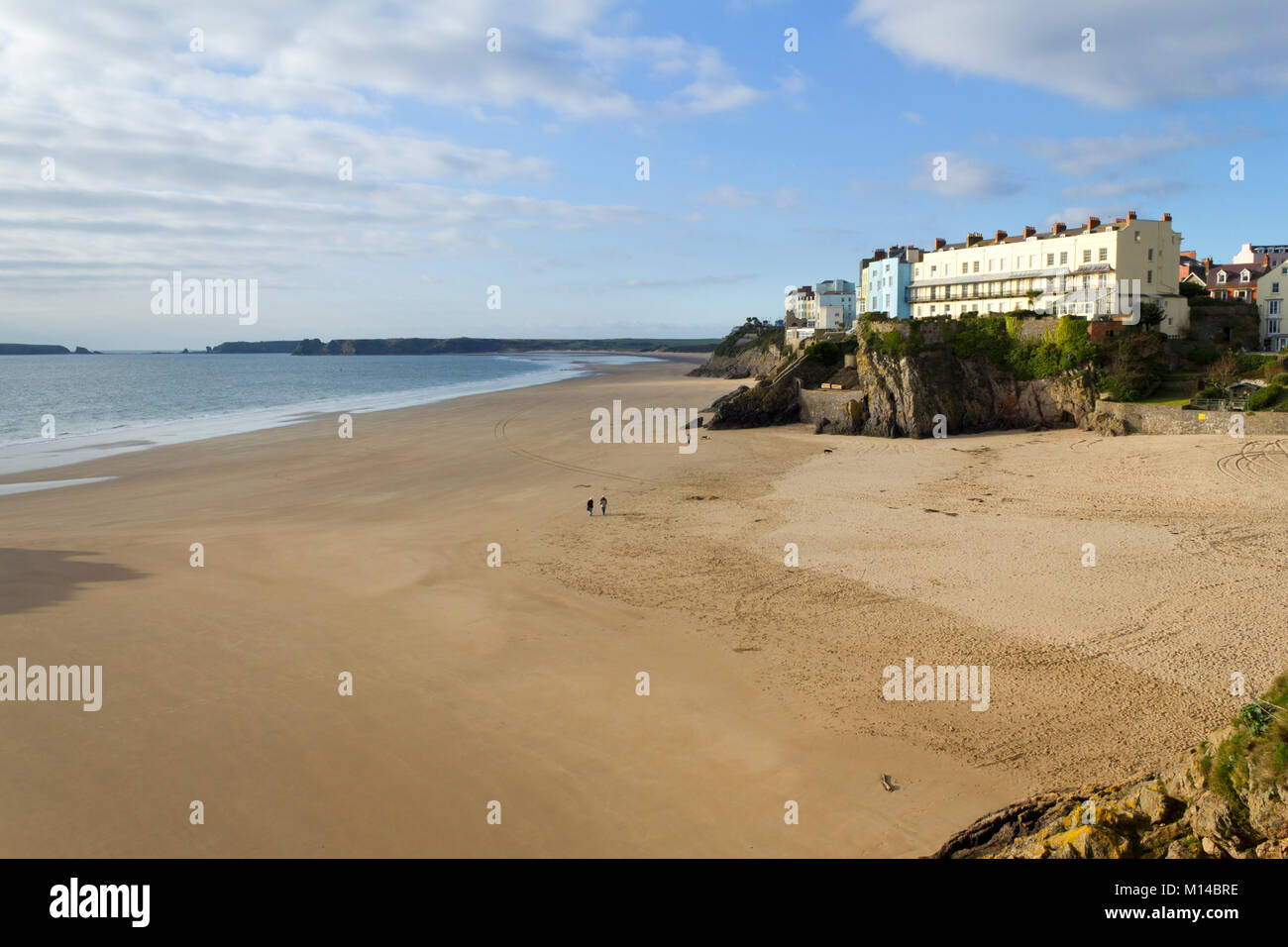 Tenby, UK - 7th November 2011: A couple walk out in November sunshine on an empty Castle Beach at Tenby, Pembrokeshire, Wales, UK. Tenby experiences a maritime climate with cool summers and mild winters and is one of the sunnier locations in Wales. Stock Photo