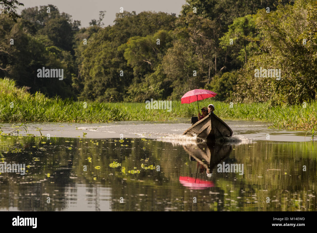 In an area with no roads the rivers are the best mode of transportation.  This family travels along the river with an umbrella to protect from the sun. Stock Photo