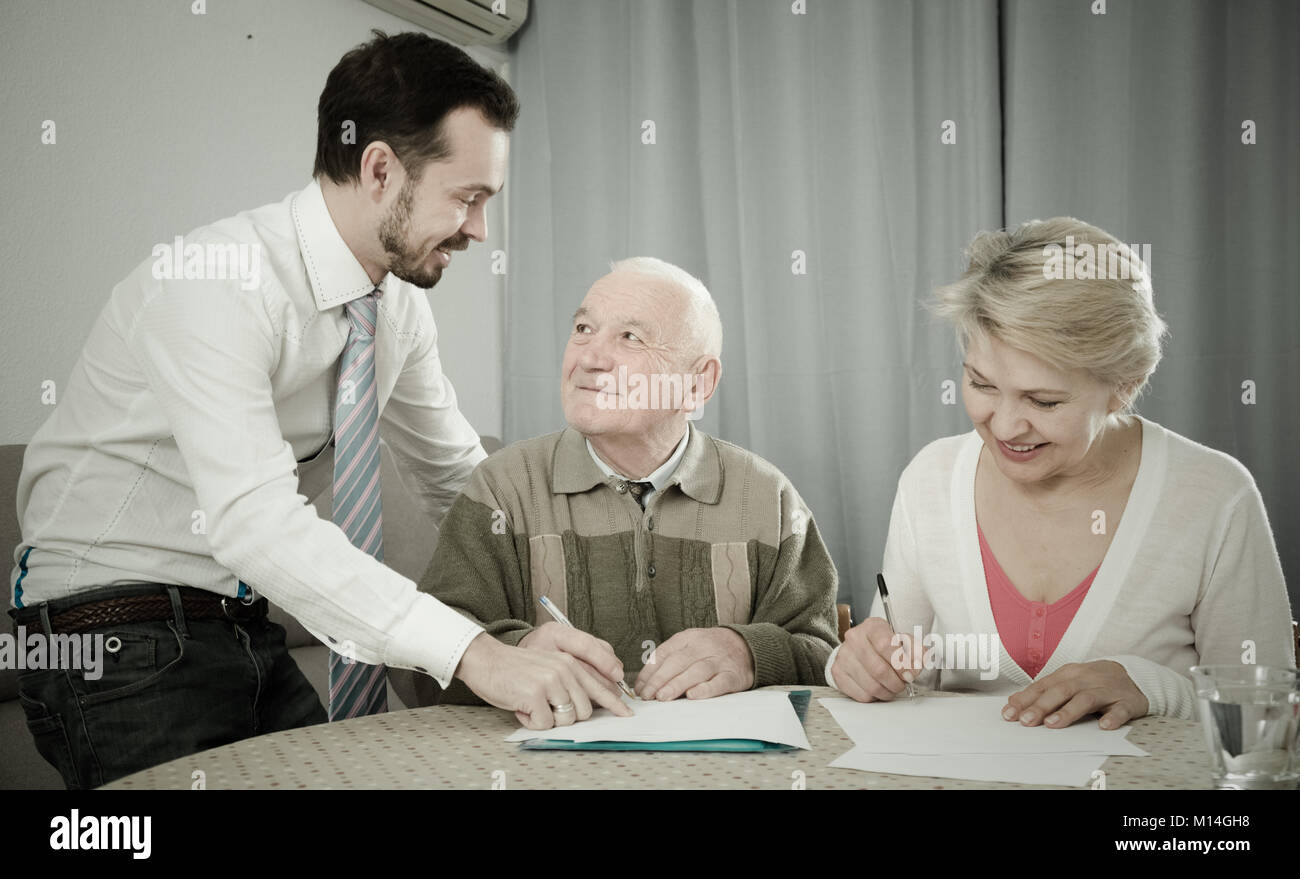 ature woman and her eldery father signing contract with smiling sales manager at home Stock Photo