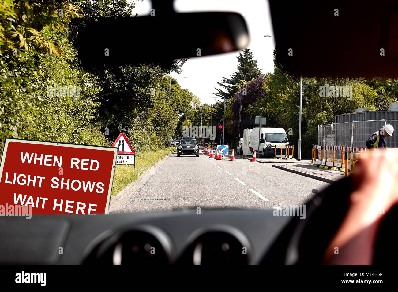 A view through the windscreen of a vehicle waiting at a red roadworks traffic light Stock Photo