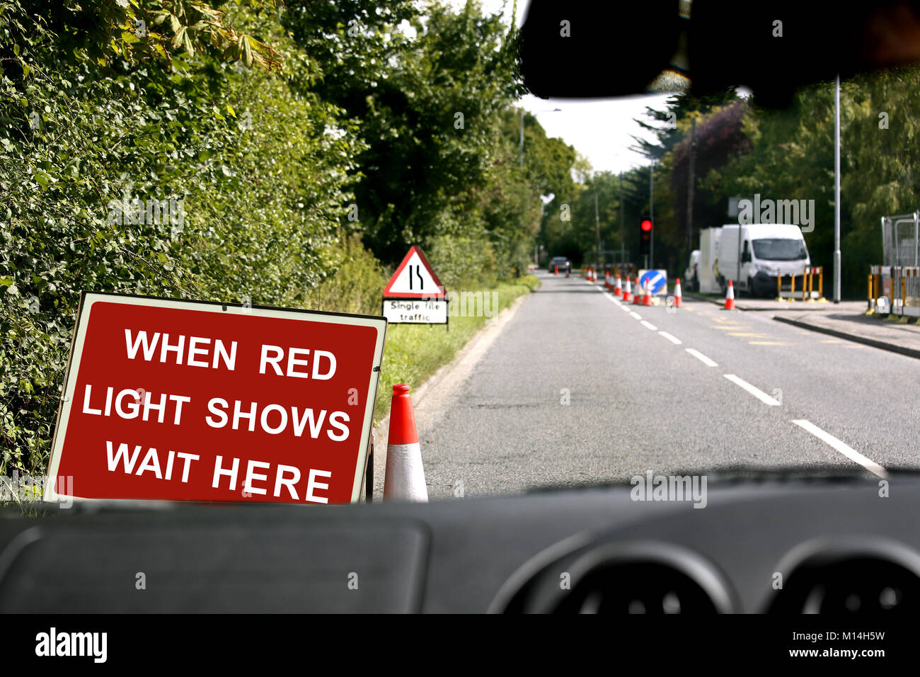 A view through the windscreen of a vehicle waiting at a red roadworks traffic light Stock Photo