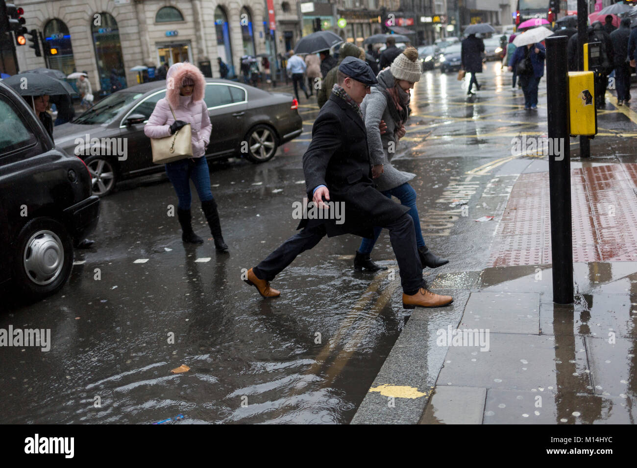 London, 24th January 2018: Storm Georgina swept across parts of Britain and in central London, lunchtime office workers were caught out by torrential rain and high winds. Pedestrians resorted to leaping across deep puddles at the junction of New Oxford Street and Kingsway at Holborn. Credit: Richard Baker / Alamy Live News. Stock Photo