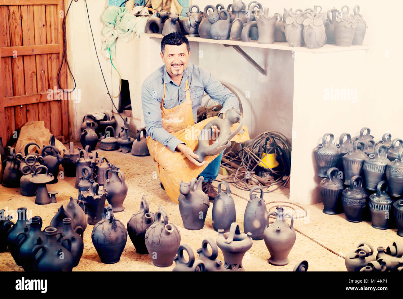 Portrait of mature male artisan with black-glazed ceramic vases in atelier Stock Photo
