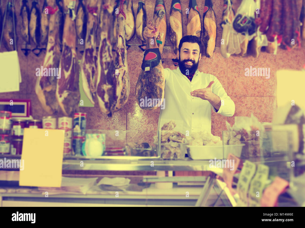 Male Shop Assistant Demonstrating Spanish Jamon In Butchers Shop Stock