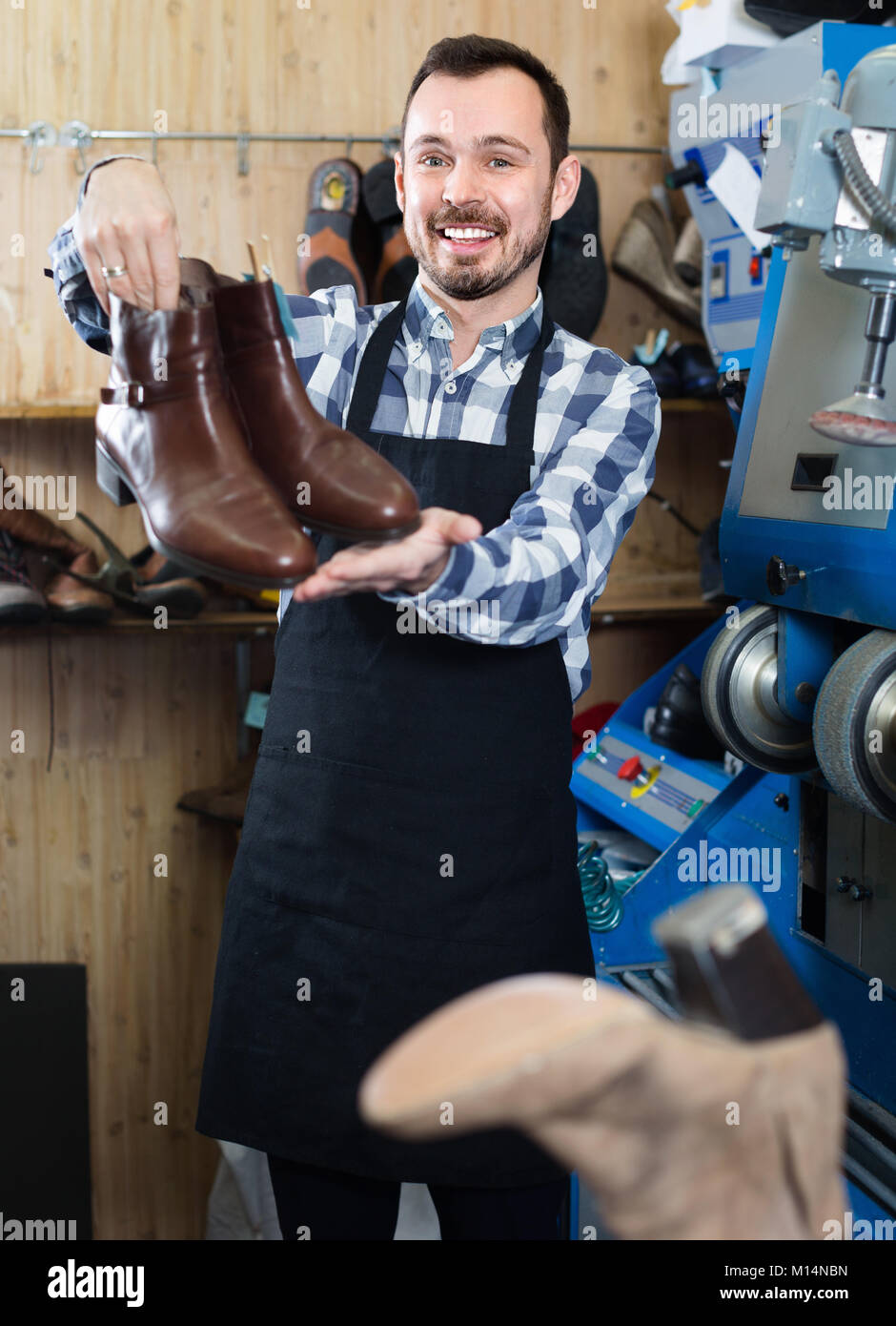 Glad male worker demonstrating repaired shoes in shoe repair