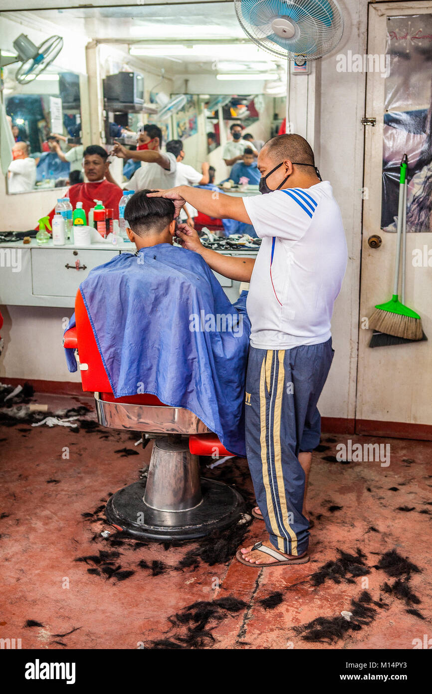 A Filipino barber cuts a high and tight fade hairstyle on a young man in Barretto, Luzon, Philippines. Stock Photo