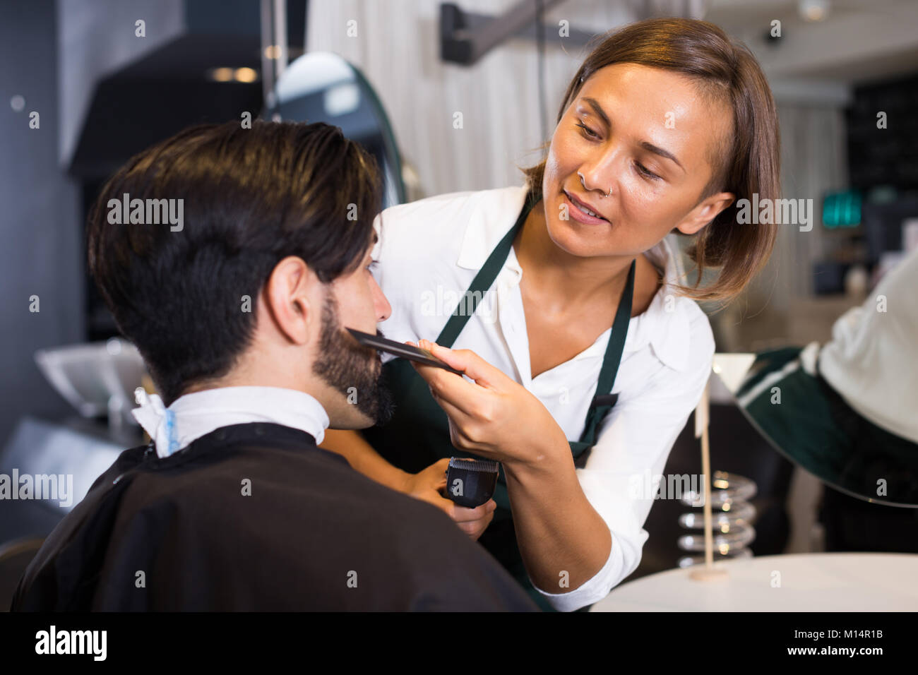 portrait of woman hairdresser shaving man's beard in Stock