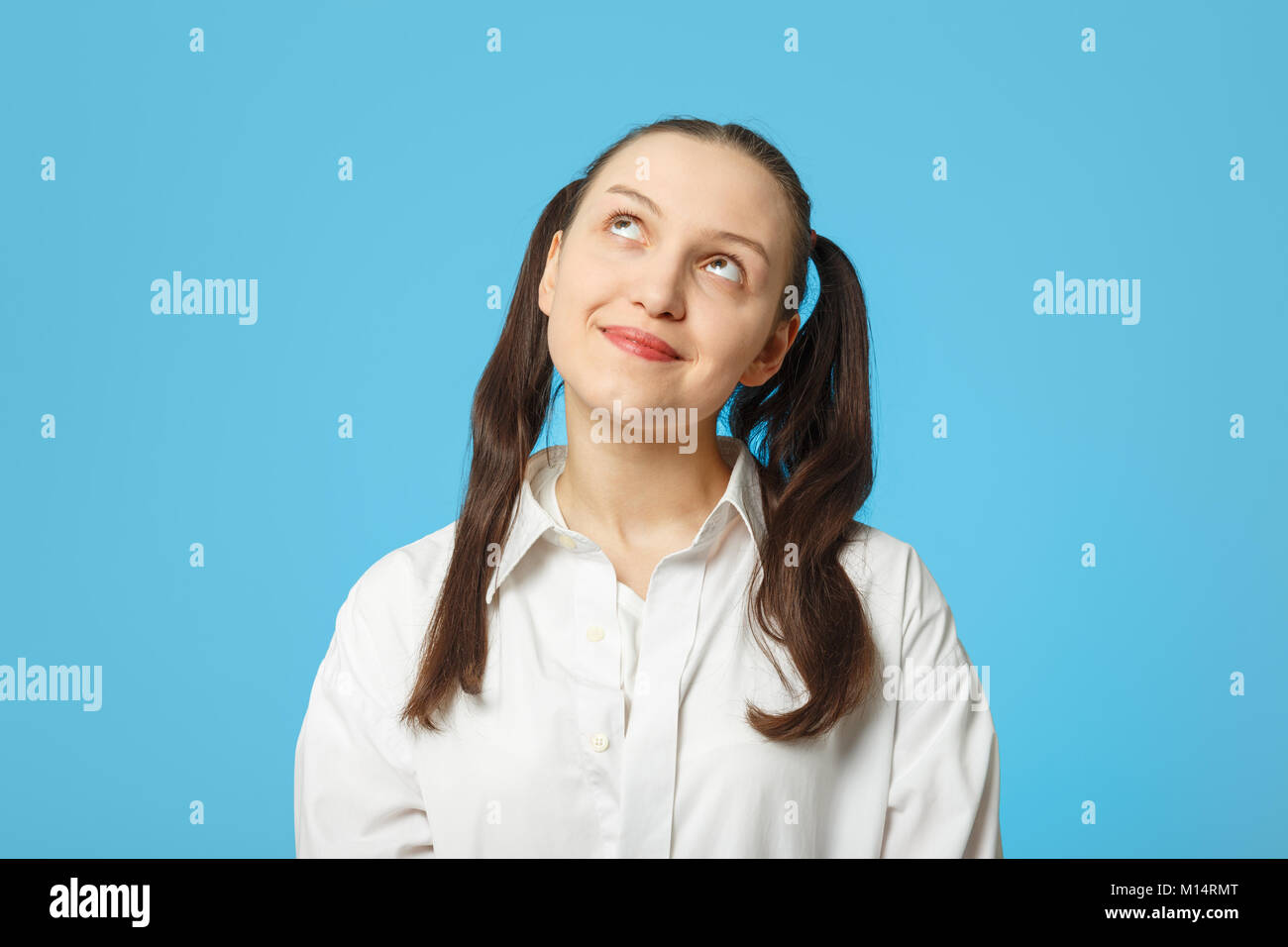 sly girl thinker on blue background looking up Stock Photo