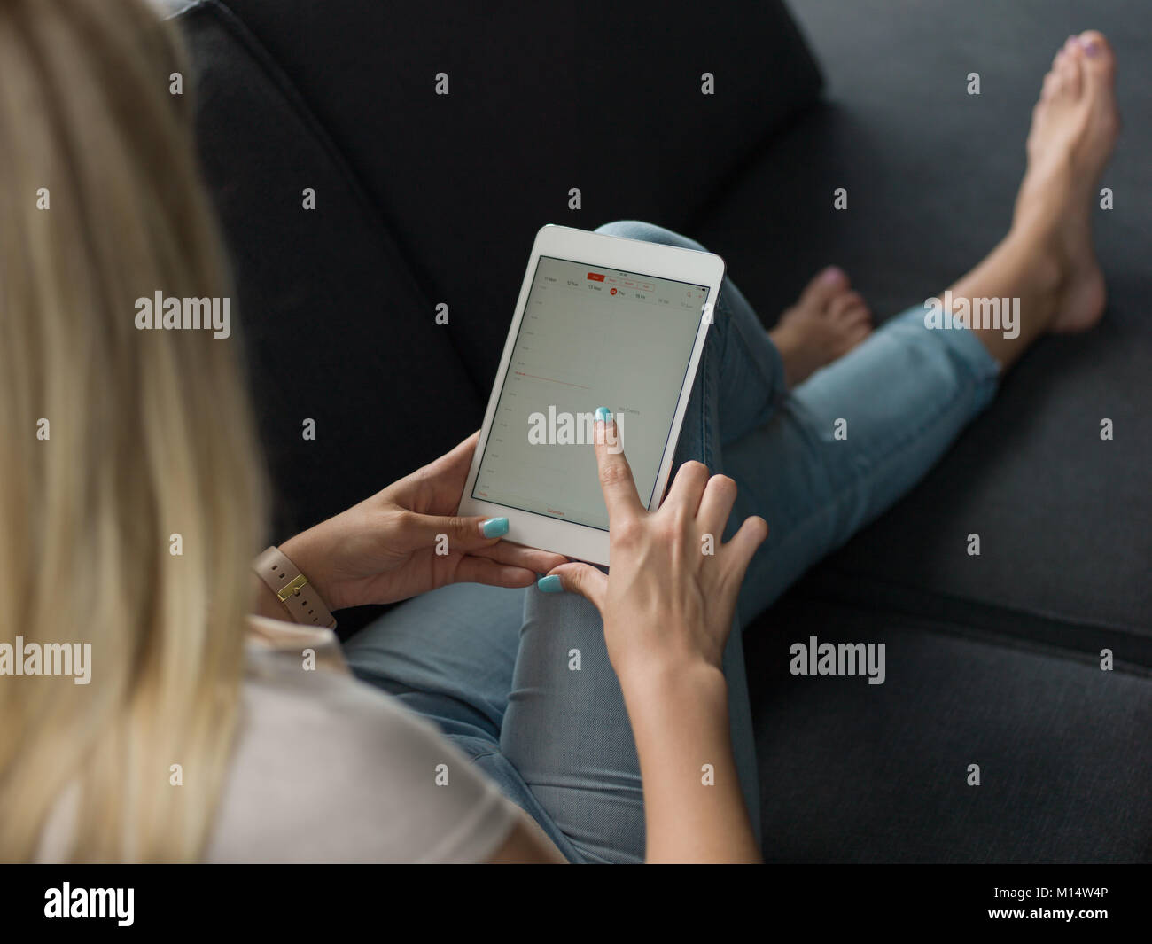 beautiful young woman on sofa at home surfing internet using tablet ...