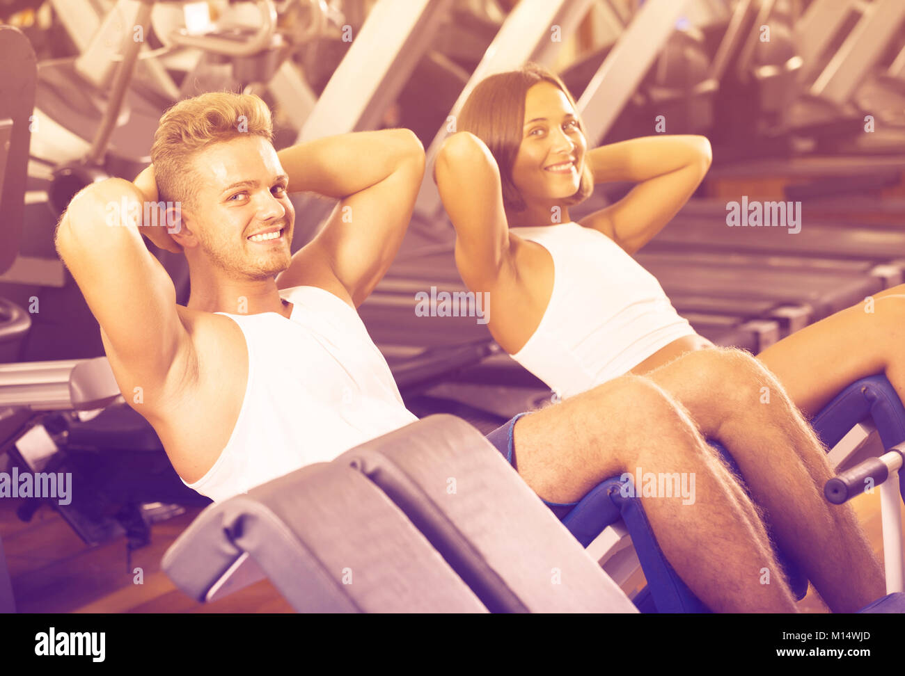 young spanish man and woman making sit ups together using machine in