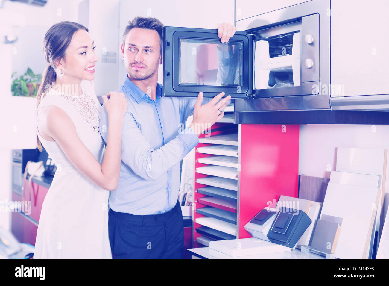 Young husband and wife are choosing new microwave in kitchen furnishing store. Stock Photo
