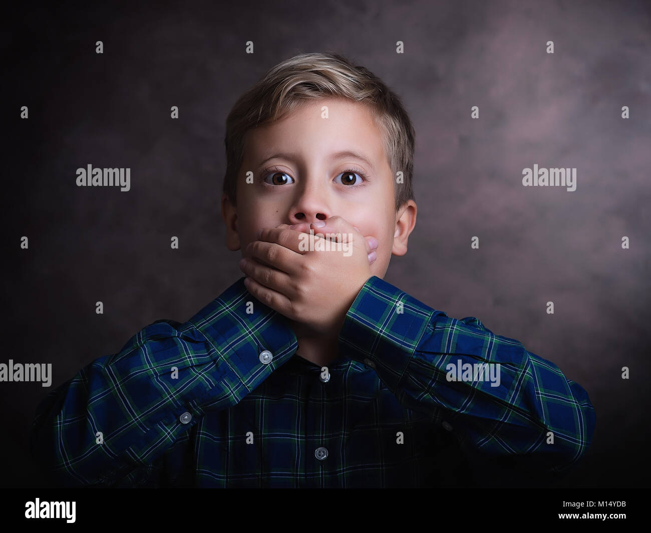 Portrait of cute little boy closed mouth with his hand, studio shot Stock Photo