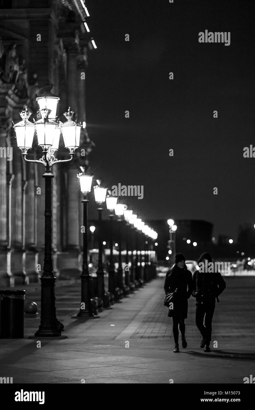 Urban scene with romantic couple walking at night on an illuminated street near an old landmark during city-break in Paris Stock Photo