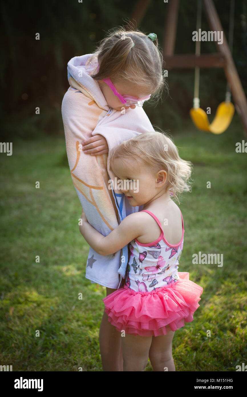 Child wrapped in towel being hugged by smaller child in swimming
