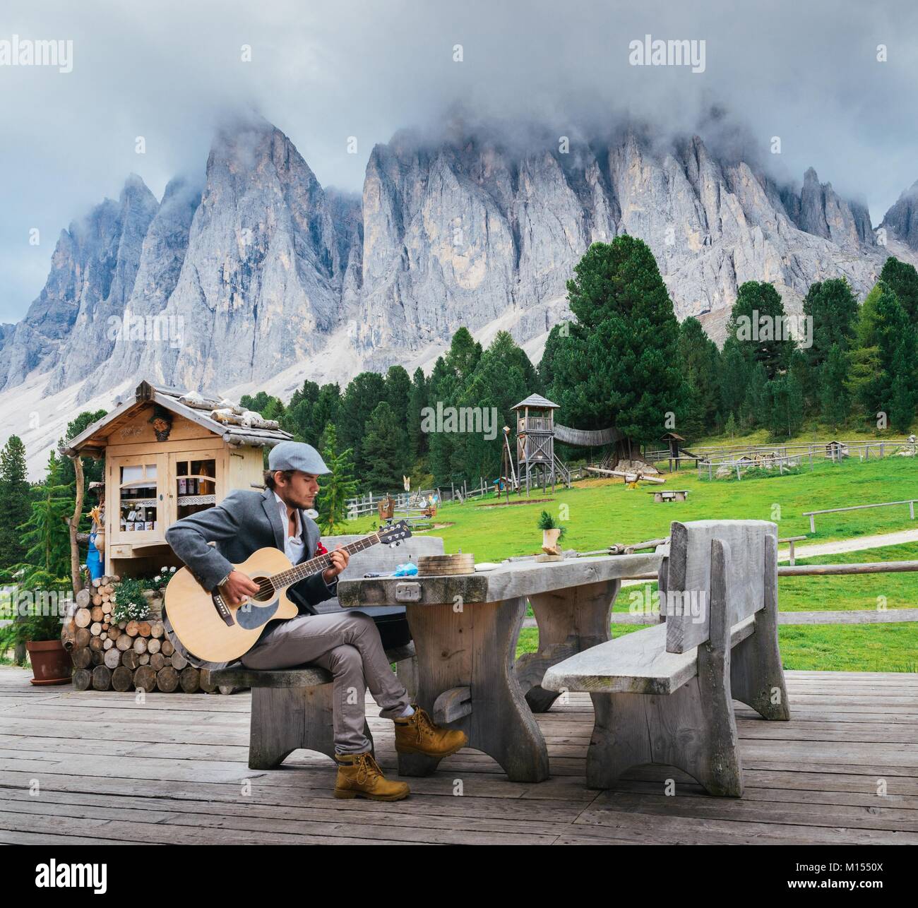 Dolomites, Italy - September 9th, 2017: Young well-dressed man 30-35 playing a guitar with Italian Dolomites rock formation background Stock Photo