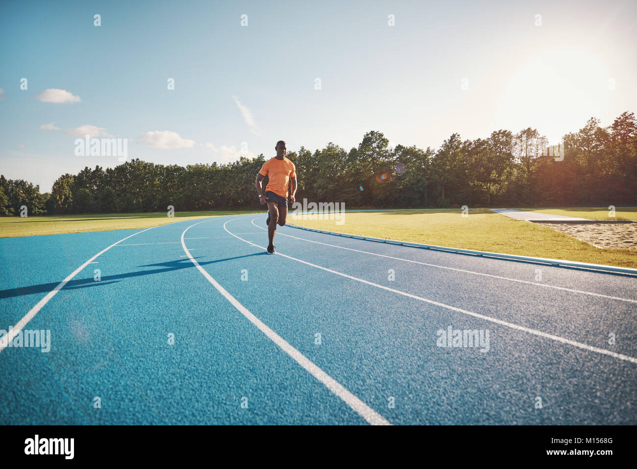Focused young African male runner in sportswear racing alone along a running track on a sunny day Stock Photo
