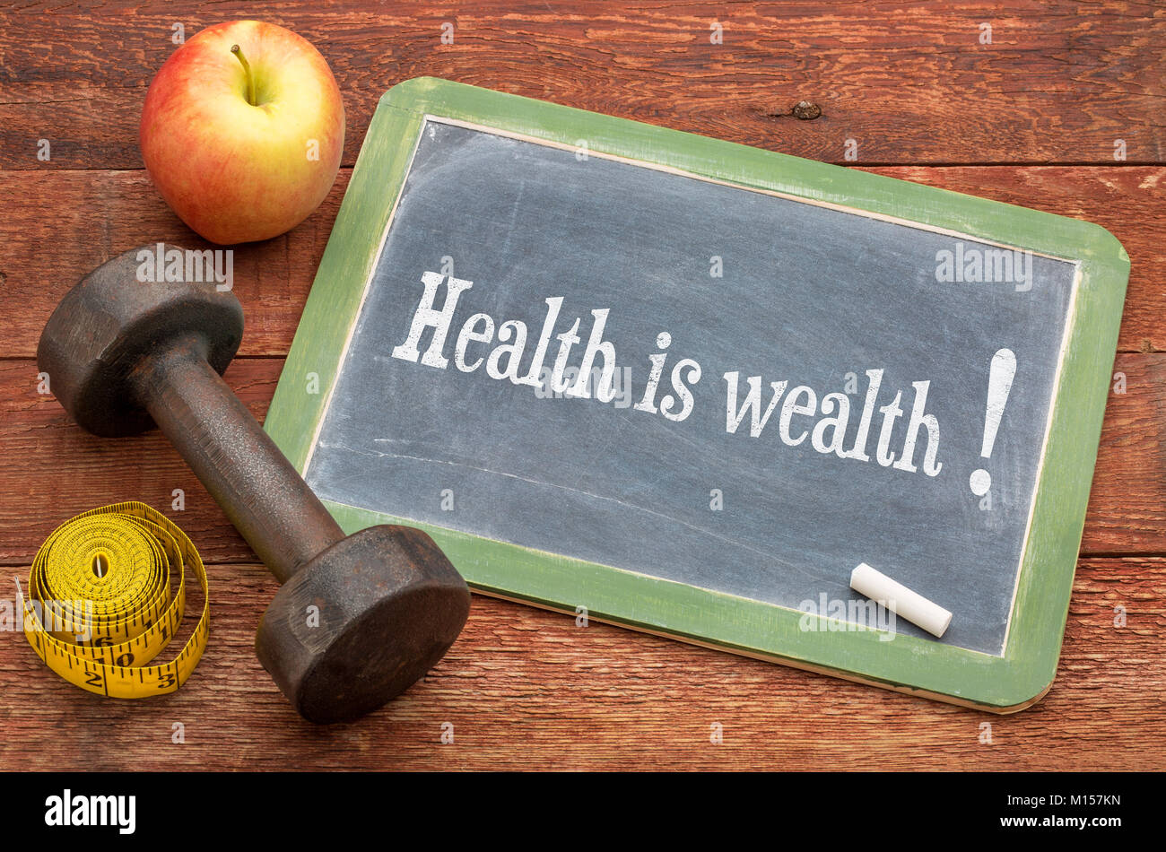 health is wealth concept -  slate blackboard sign against weathered red painted barn wood with a dumbbell, apple and tape measure Stock Photo
