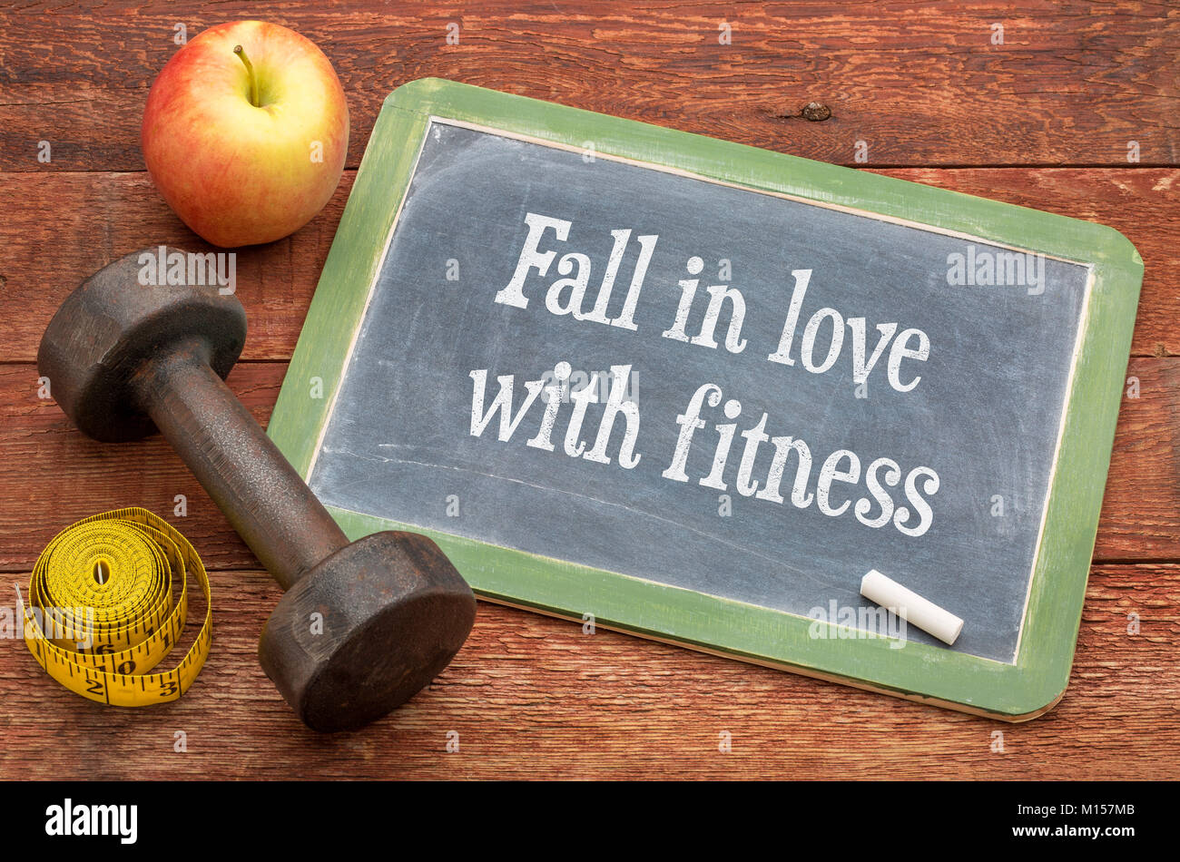 fall in love with fitness -  slate blackboard sign against weathered red painted barn wood with a dumbbell, apple and tape measure Stock Photo