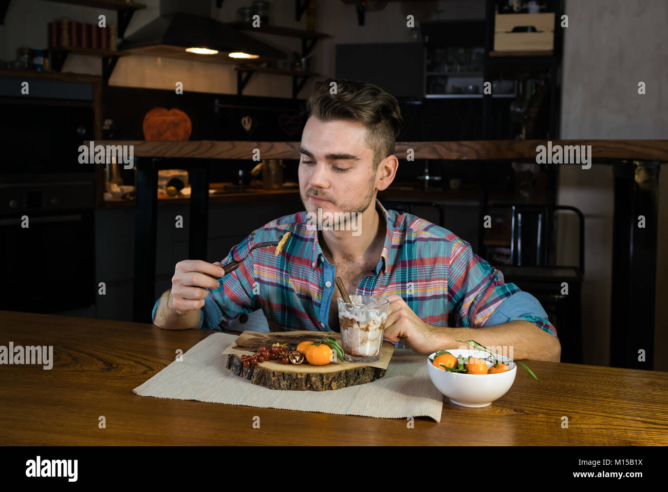 Funny hungry person eats pancakes on the breakfast. Young man sits at the table in the stylish home kitchen. The meal close to over. Stock Photo