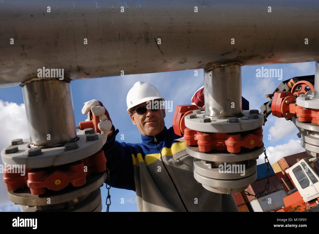 Oil and gas refinery worker turning on large pipelines. Stock Photo