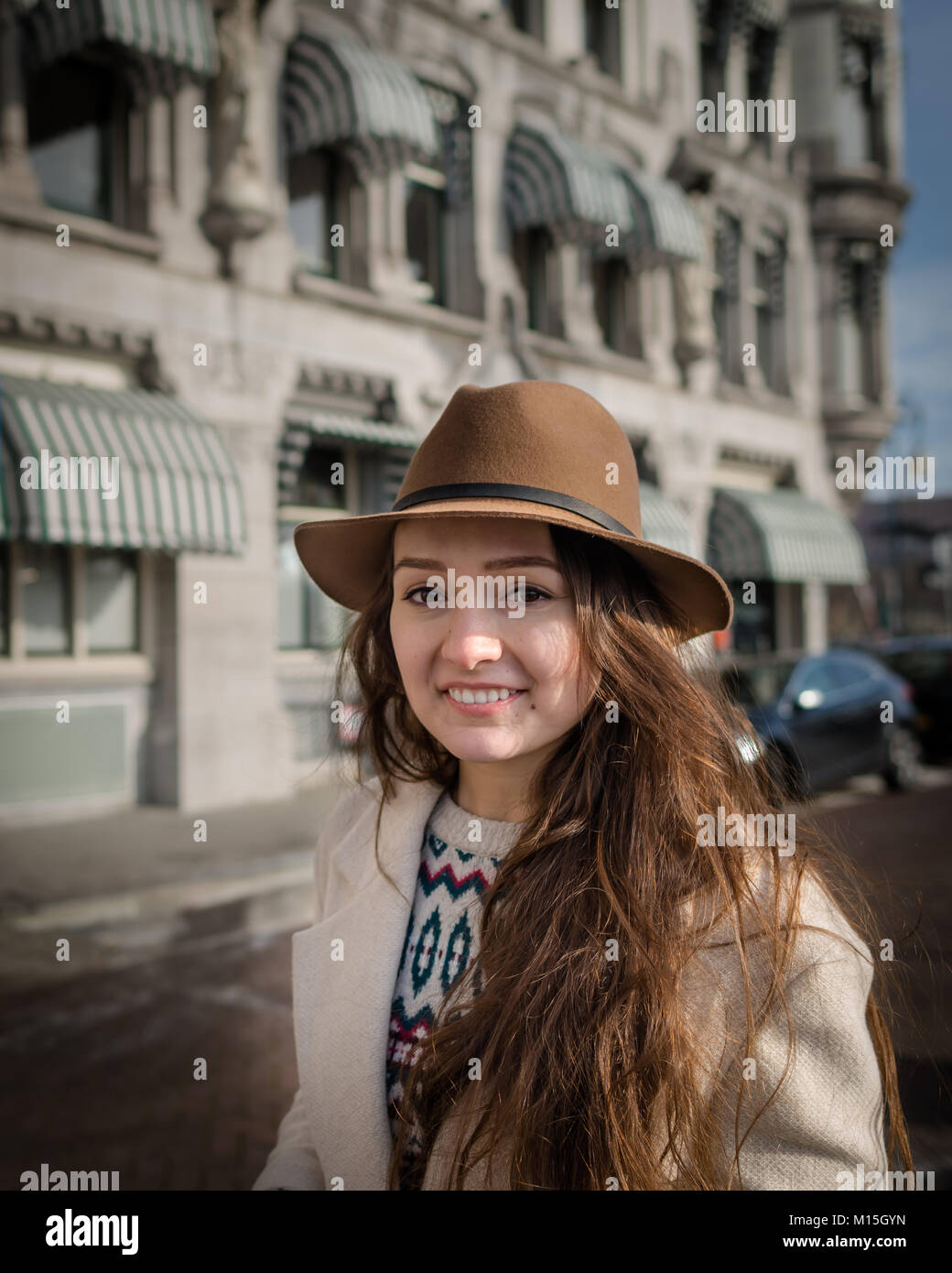Portrait of a young female tourist with elegant hat and coat exploring the city. Trendy woman traveler with smile touring old town Stock Photo