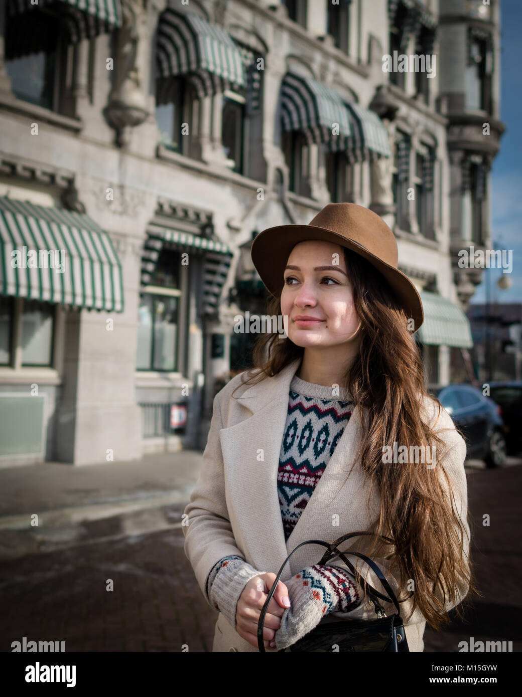Young female tourist with elegant clothes walking in the city. Trendy woman traveler with smile looking on buildings and touring old town Stock Photo