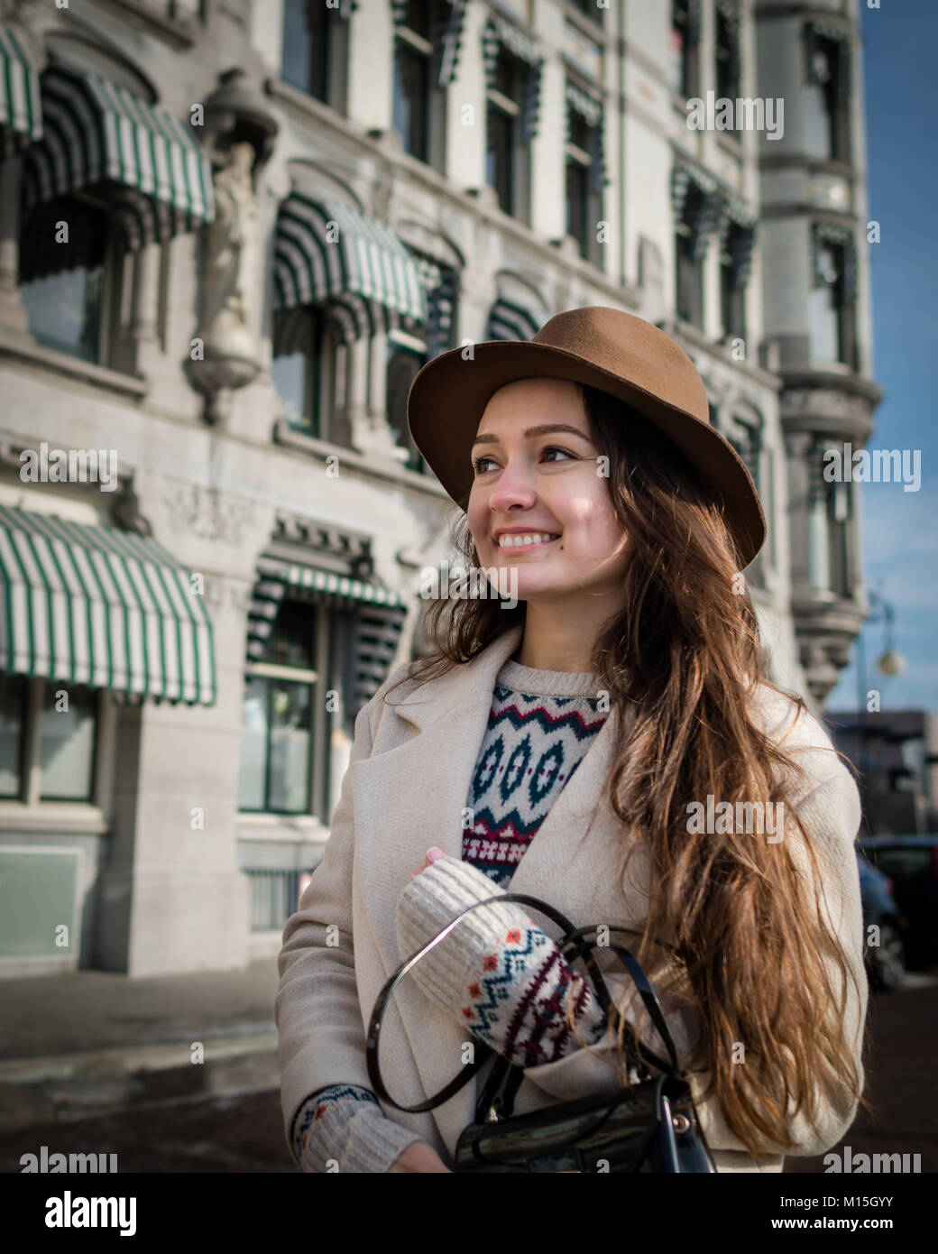 Portrait of a young female tourist with elegant clothes exploring the city. Trendy woman traveler with smile looking on buildings and touring old town Stock Photo