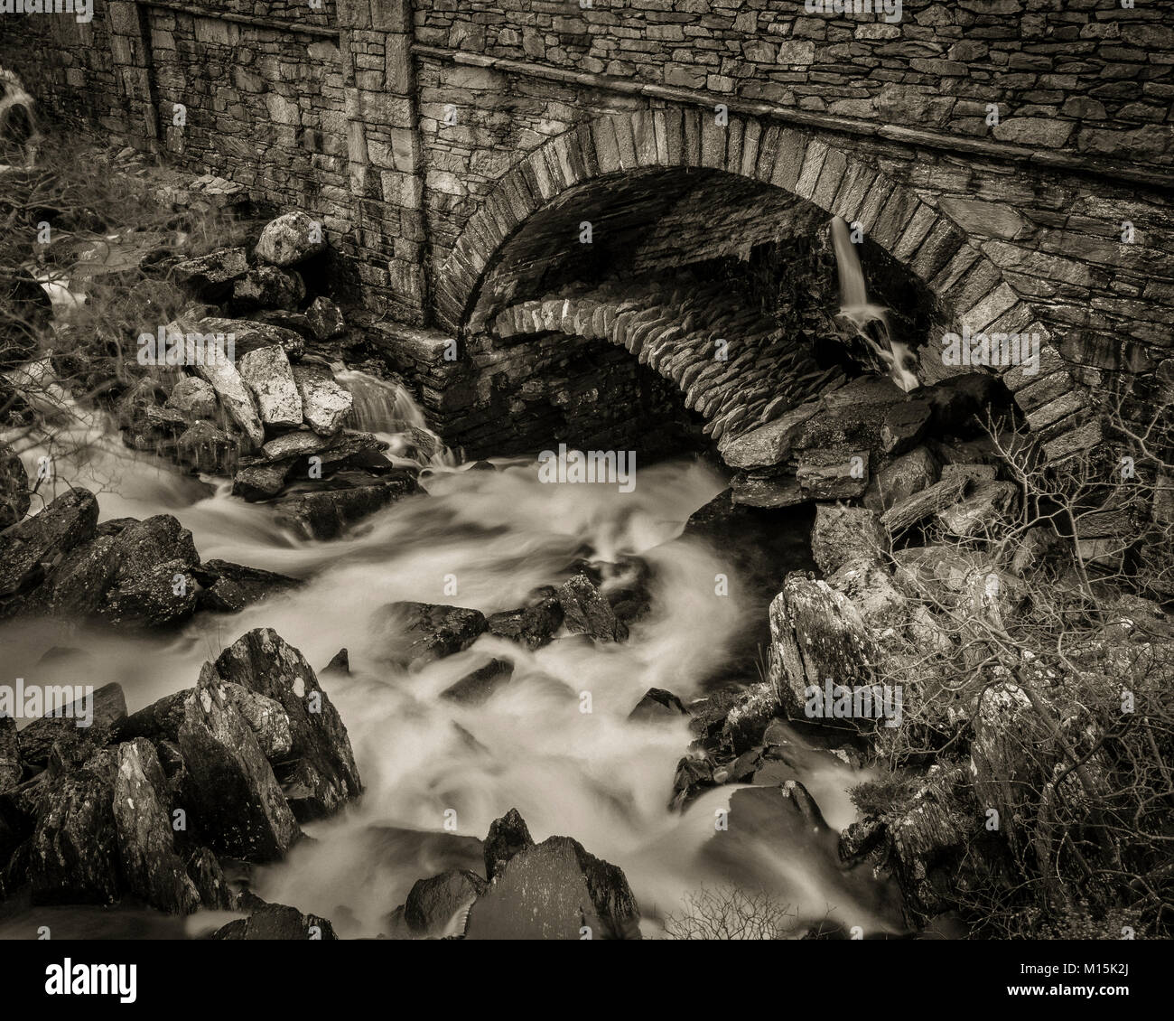 Stream flowing under ancient stone arch bridge Pont Pen-y-Benglog, Snowdonia, Wales Stock Photo
