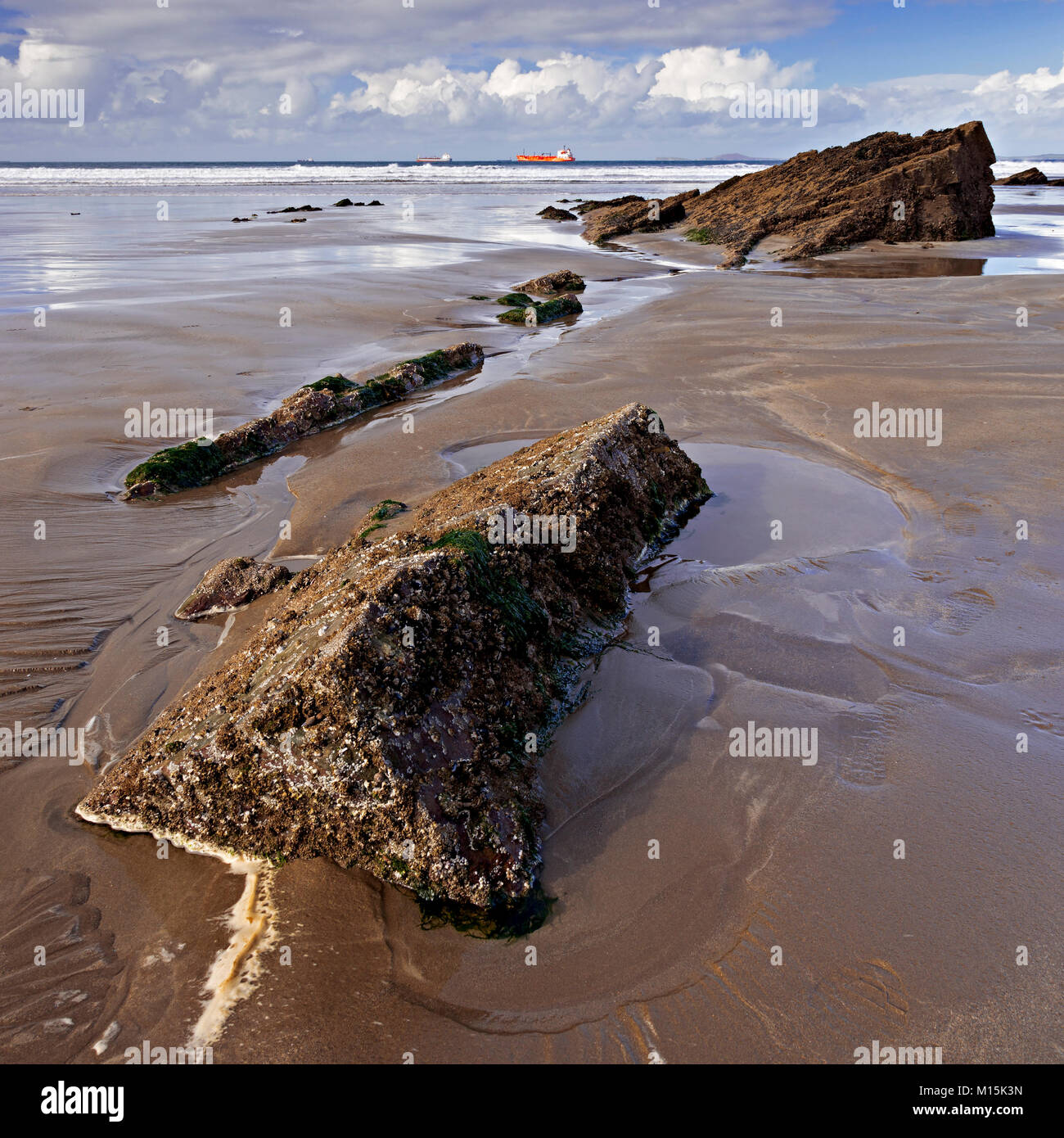 Rocks in wet sand on the beach at Broad Haven on the Welsh coast with a tanker on the horizon Stock Photo